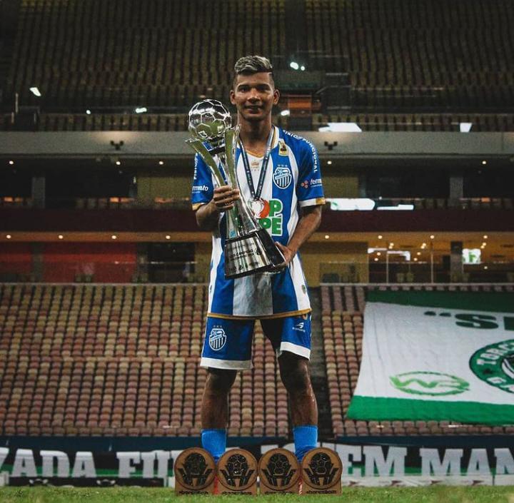 Jogador Edison Negueba segura troféu do Campeonato Amazonense. Ele usa um uniforme com camisa listrada em azul e branco e calção azul