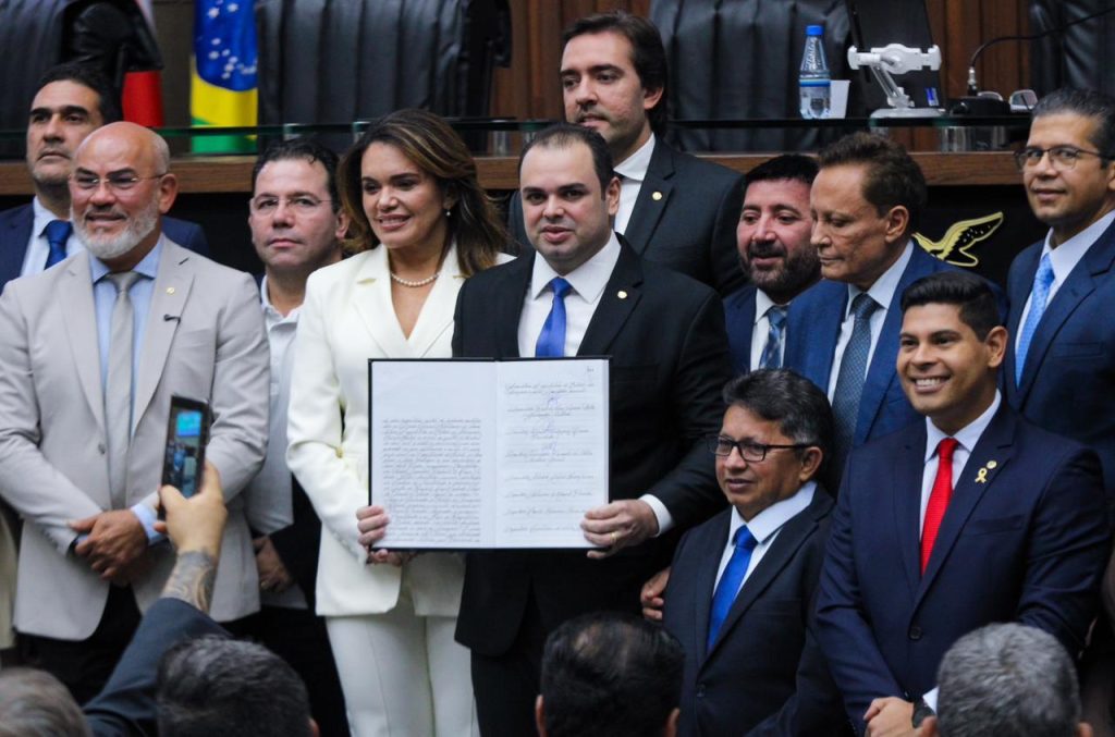 Deputados reunidos. Todos vestem roupas sociais. Ao centro, Roberto Cidade segura o diploma de posse