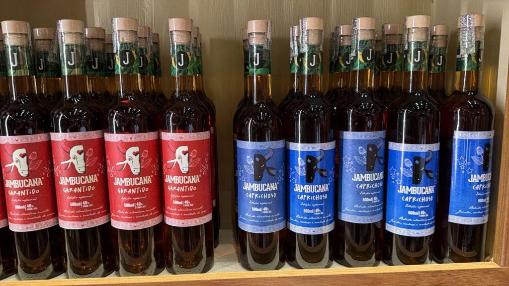 Imagem de garrafas de vidro contendo cachaça de jambu. Metade das garrafas têm o rótulo vermelho e imagem do Boi Garantido e a outra metade, azul, com imagem do Boi Caprichoso