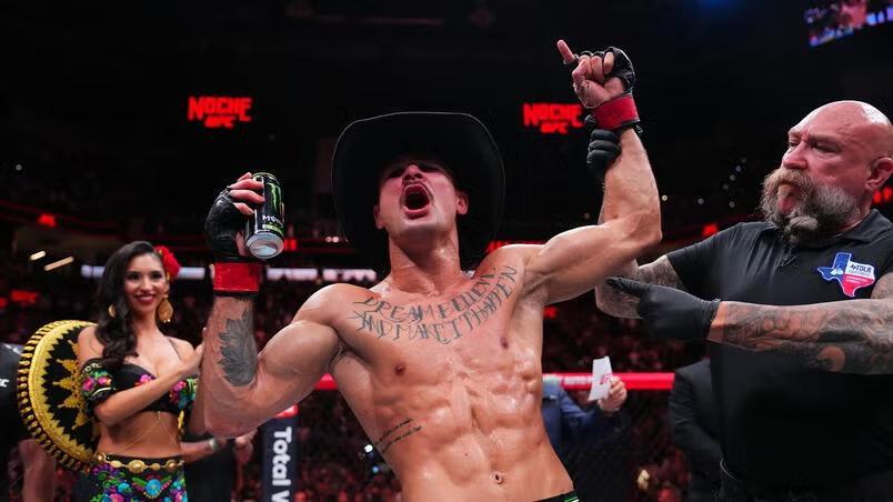 Imagem do lutador Diego Lopes. Ele usa um chapéu de cowboy, tradicional no México. Ele segura uma lata de energético com a mão direita enquanto a esquerda é erguida pelo juiz da luta e ele aponta para o céu com o dedo indicador. Diego é branco, está sem camisa e tem uma tatuagem no peito, próximo aos ombros